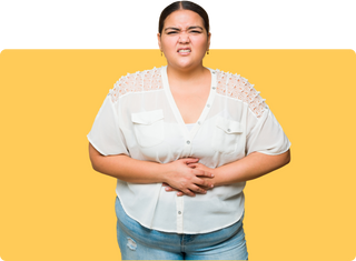 Woman in a white top grimacing and holding her stomach against a yellow background