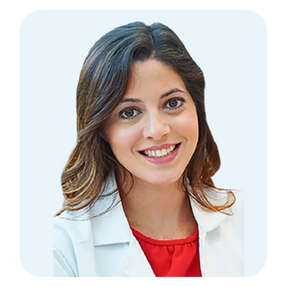 A smiling woman with brown hair wearing a white lab coat over a red top, shown in a clean studio-style portrait with a light blue rounded square background.