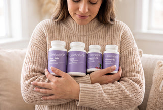A woman in a beige knit sweater holds four white supplement bottles with purple labels against her chest. The bottles are branded Celebrate Health and include Hair, Skin & Nails, Sleep, and Vitamin B3.
