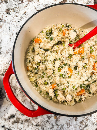 Red pot with cauliflower rice and vegetables on a speckled countertop