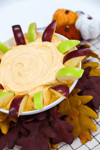 Dip in a bowl with fruit and dip on a decorative leafy background